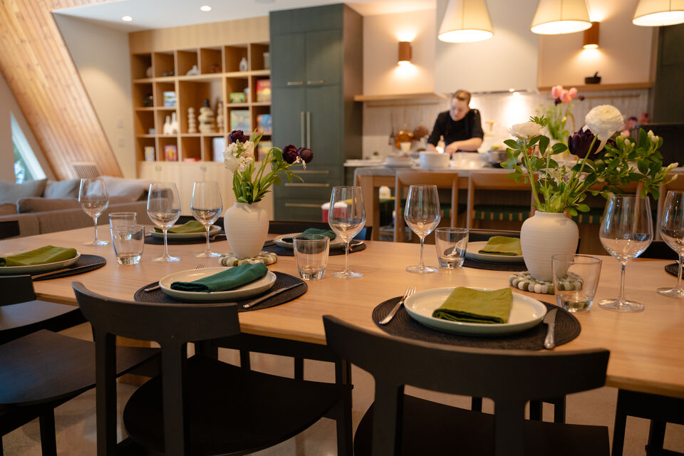 The table set in green linens while the chef cooks at the range behind