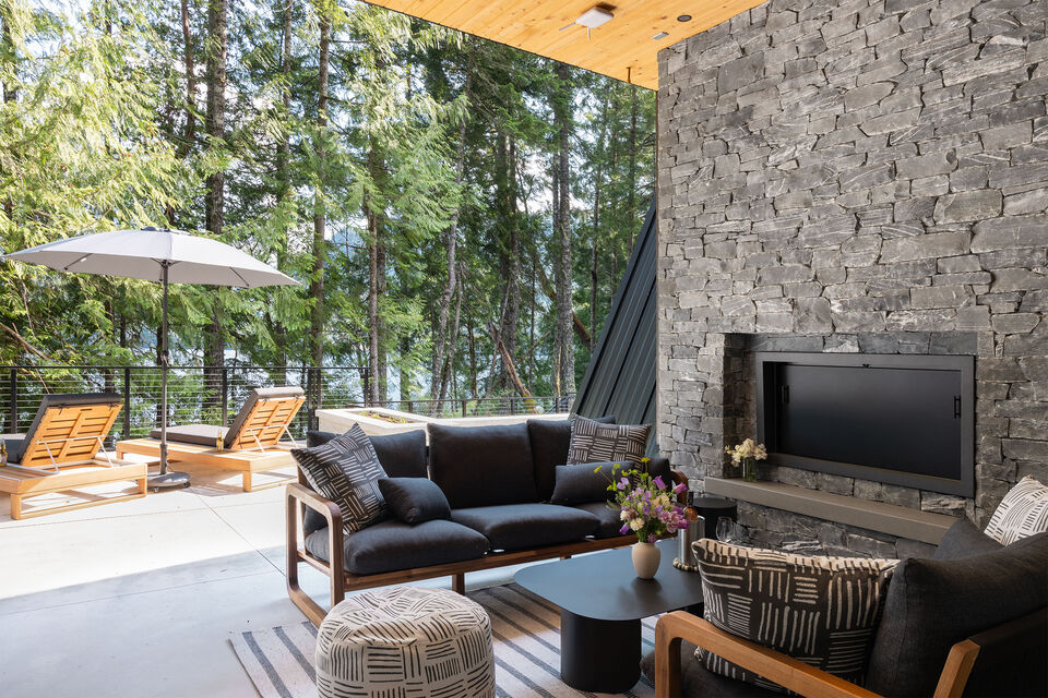 The outdoor lounge with stone fireplace and sun loungers among the firs