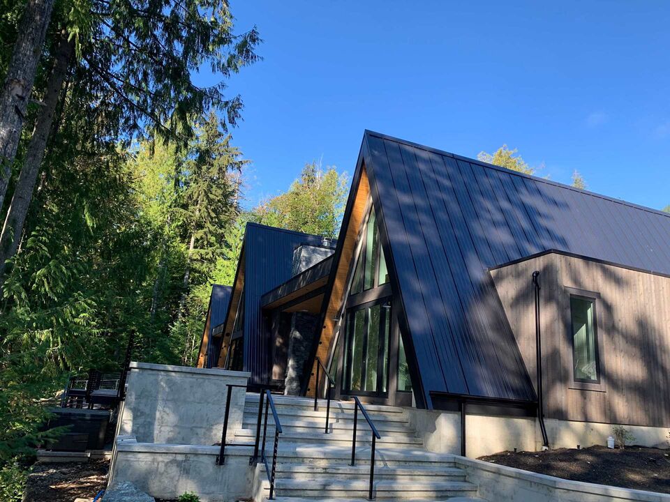 Rear exterior of the Main Cabin with dark standing-seam metal roof against blue sky and fir trees
