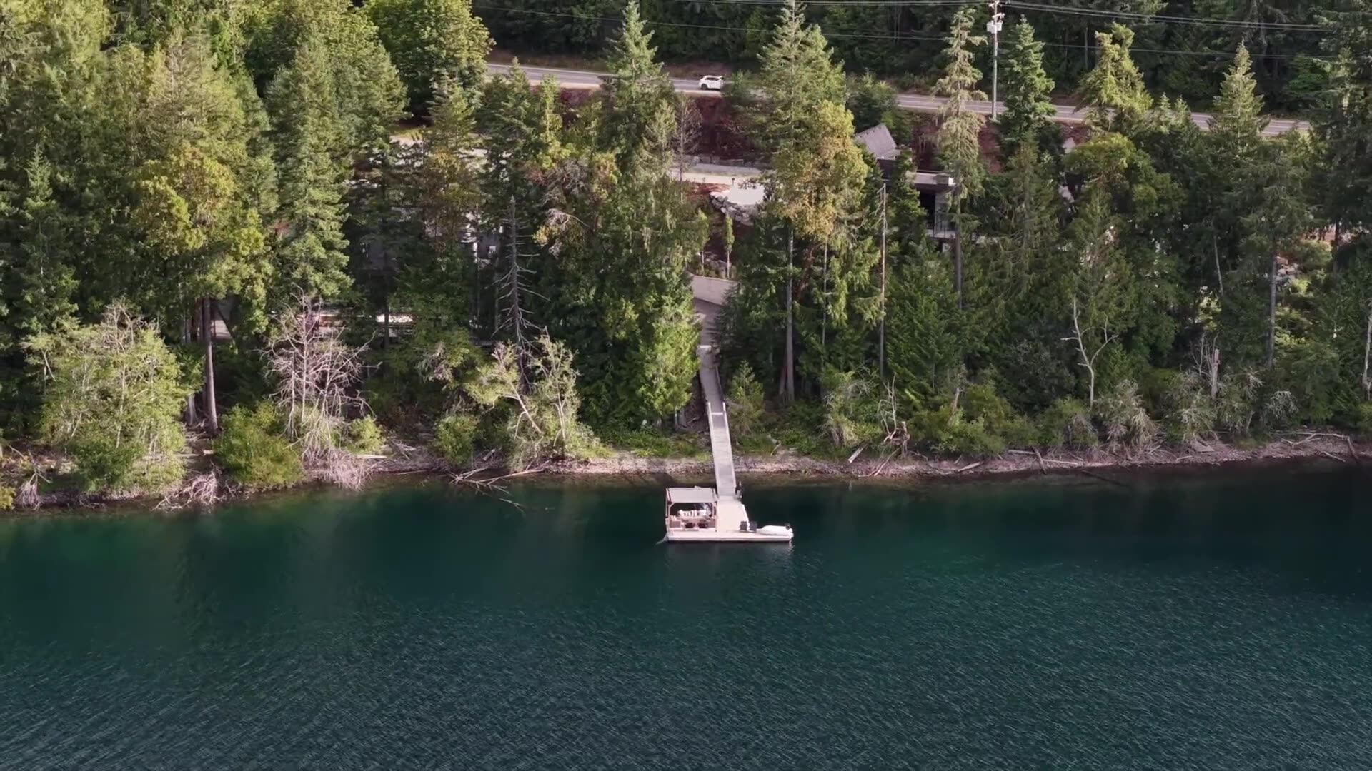Drone view descending over the private dock and forested shoreline at Youbou