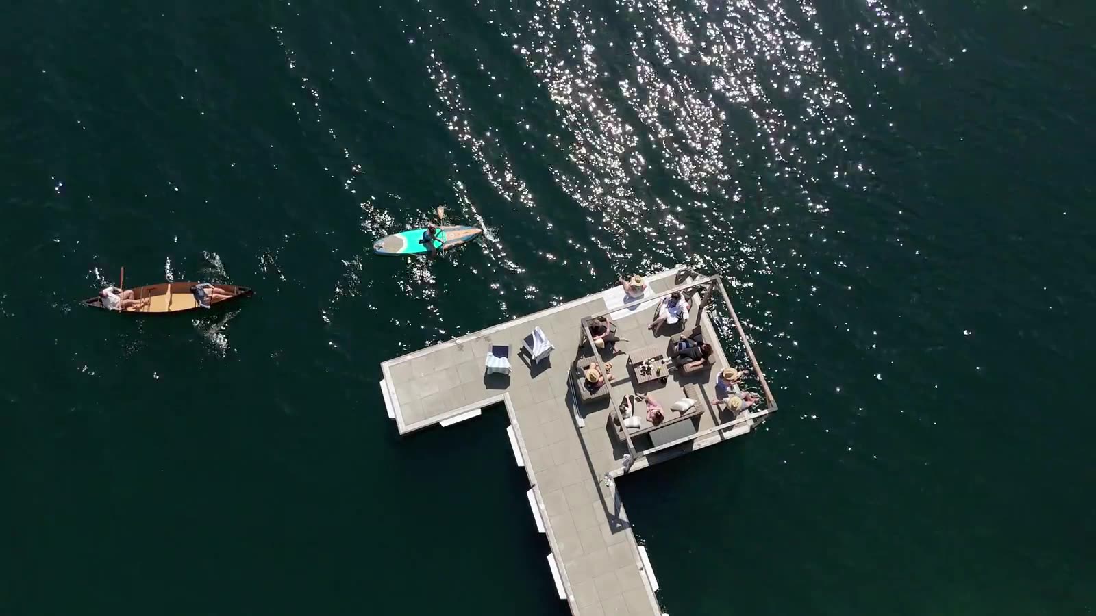 Drone view straight down on the dock set for dinner as a canoe and paddleboarder drift past