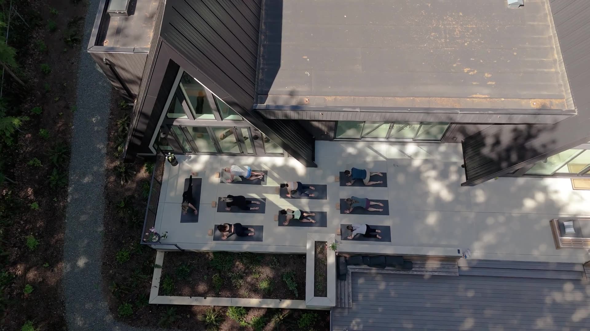 Drone view of a yoga class flowing on the terrace beneath the A-frame