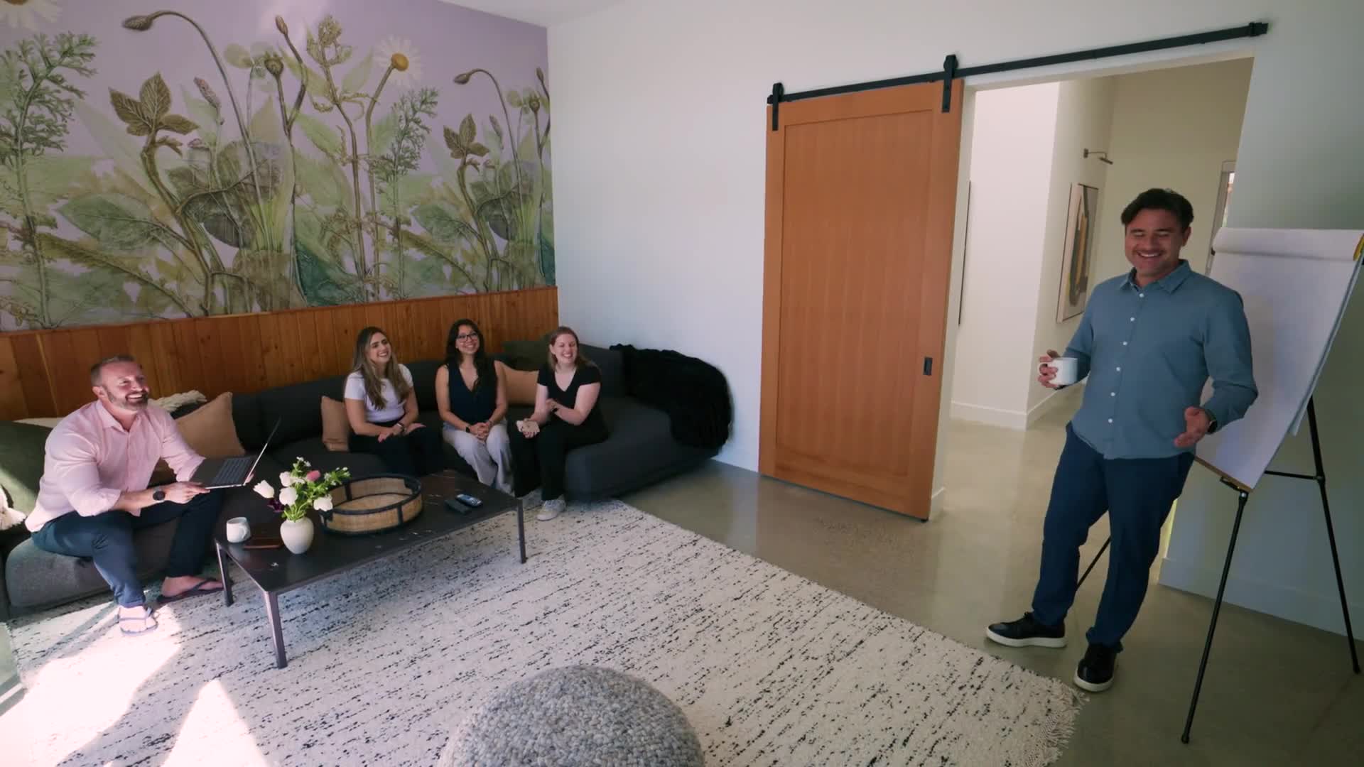 A facilitator leads a workshop from the flipchart while the team gathers in the lounge